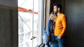 Glueckliches Paar schaut aus dem Fenster ihres Wohneigentums, welches sich noch im Bau befindet.